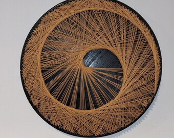 May include: A circular wall hanging with a black background and a spiral design created with brown string.