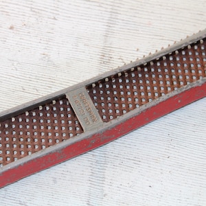 May include: A red and silver hand plane with a metal grid surface. The plane is labeled "CRAFTSMAN 2 67721 DD".
