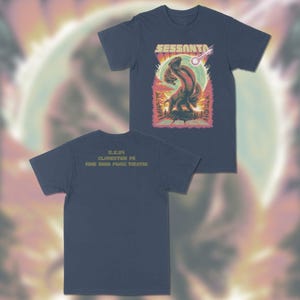 May include: Navy blue t-shirts with a colorful graphic design. The front of the shirt features the word "Sessanta" above a two-headed creature with a meteor. The back of the shirt has the text "5.2.24 Clarkston MI Pine Knob Music Theatre."