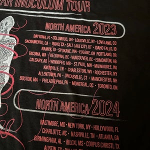 May include: Black t-shirt with white text that reads "TOOL EAR INOCULUM TOUR" and lists tour dates for North America in 2023 and 2024.