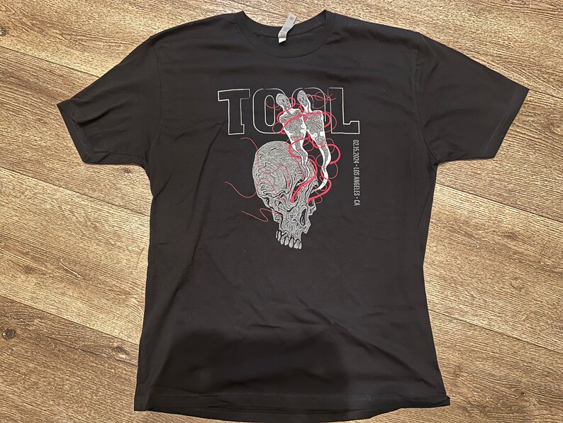 May include: Black t-shirt with a white graphic of a skull with red lines and the word "TOOL" above it. The text "02.15.2023 - LOS ANGELES - CA" is printed below the skull.