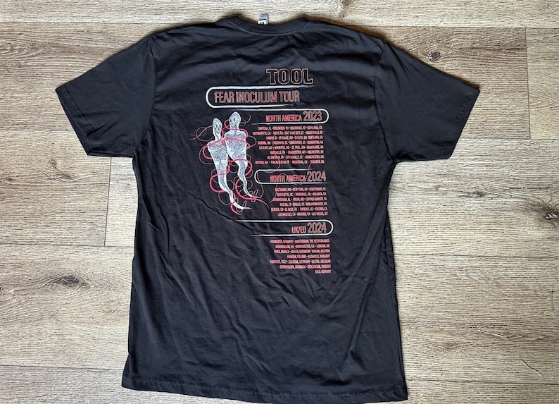 May include: Black t-shirt with a white graphic of two figures and the text "TOOL FEAR INOCULUM TOUR" with tour dates for North America and the UK in 2023 and 2024.