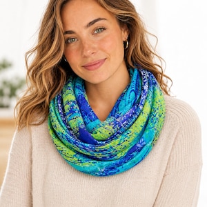May include: A colourful infinity scarf in shades of blue and green. The scarf has a watercolour-like pattern with splashes of turquoise, royal blue, and lime green. The scarf is wrapped around the neck.