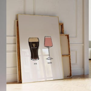 May include: A framed print featuring two illustrated glasses: a pint of Guinness and a wine glass. The Guinness glass is dark with a white head, and the wine glass is filled with pink liquid. The words "HIS" and "HERS" are below the glasses.