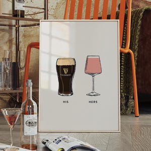 May include: A framed print featuring illustrations of a pint of Guinness and a stemmed glass of pink wine, labeled "HIS" and "HERS". The print is displayed on a wooden floor, with a bar cart and furniture in the background.