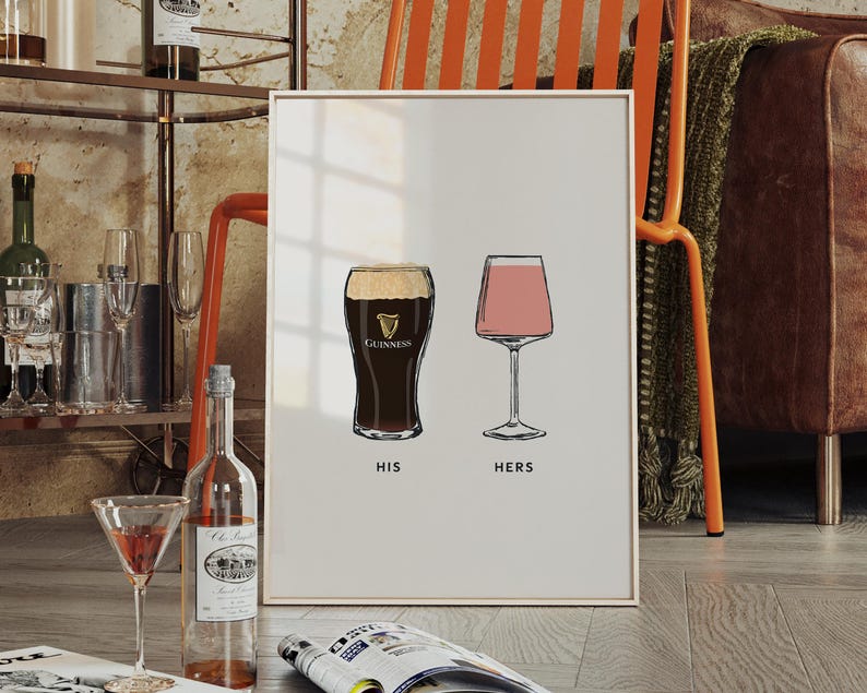 May include: A framed print featuring illustrations of a pint of Guinness and a stemmed glass of pink wine, labeled "HIS" and "HERS". The print is displayed on a wooden floor, with a bar cart and furniture in the background.