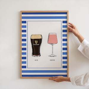 Puede incluir: Impresión enmarcada con ilustraciones de una pinta de Guinness y una copa de cóctel rosa. La impresión tiene un borde a rayas azul y blanco y las palabras "HIS" y "HERS". El marco es de color marrón claro.