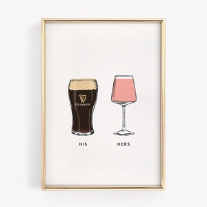 May include: A framed print featuring two illustrated glasses: a pint of Guinness and a pink cocktail. The words "HIS" and "HERS" are printed below the glasses. The print is in a gold frame.
