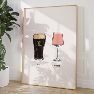 May include: A framed print featuring illustrations of two drinks: a pint of Guinness and a pink cocktail in a stemmed glass. The words "HIS" and "HERS" are printed below the respective glasses. The artwork has a minimalist style.
