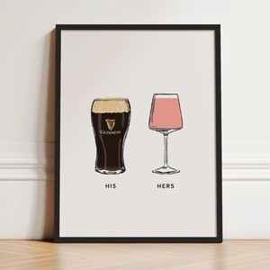 May include: Framed art print featuring two illustrated glasses: a pint of Guinness and a stemmed glass with a pink drink. The words "HIS" and "HERS" are printed below the glasses. The print is in a black frame.