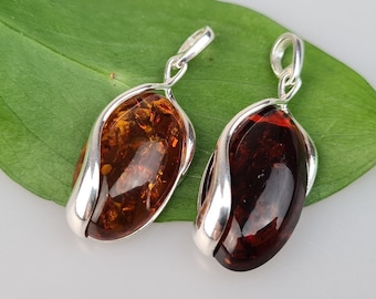 May include: Two amber pendants with silver settings. The pendants are oval shaped and have a smooth, polished finish. The amber is a rich, warm color.
