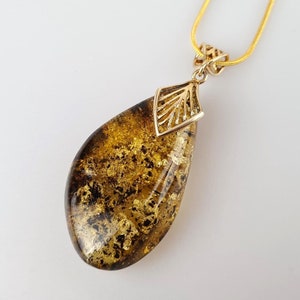 Peut inclure: Un collier en chaîne dorée avec un pendentif en ambre en forme de larme. Le pendentif est orné d'un motif en filigrane doré et est serti dans un cadre doré.