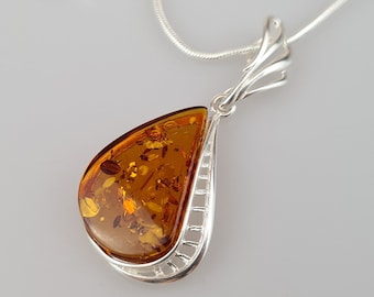 May include: A silver necklace with a teardrop-shaped amber pendant. The amber is a deep orange color and has inclusions of plant matter.