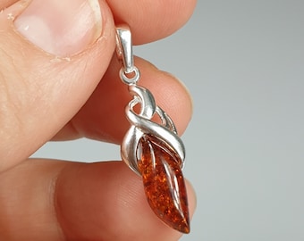 May include: A silver pendant with a teardrop-shaped amber stone. The pendant has a twisted design and is held in a hand.