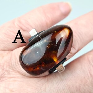 K&ouml;nnte beinhalten: Ein Ring mit einem gro&szlig;en, ovalen Bernstein, der in eine silberne Fassung gefasst ist. Der Stein ist dunkelbraun mit goldenen Einschl&uuml;ssen.