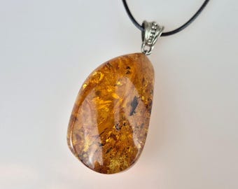 May include: A teardrop-shaped amber pendant with a silver bail, hanging from a black leather cord.