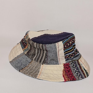 以下が含まれることがあります： さまざまな生地の柄と色を使用したパッチワークのバケットハット。クリーム色、ネイビー、赤、青、茶色の模様の生地を使用。つばの幅は約7.6cmです。