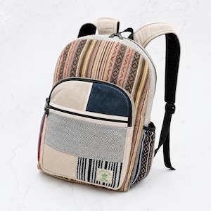 May include: A backpack featuring a patchwork design with woven fabric in stripes of tan, brown, and orange, alongside panels of blue and black-and-white herringbone. It includes a front zippered pocket and a label with a green leaf icon and text.
