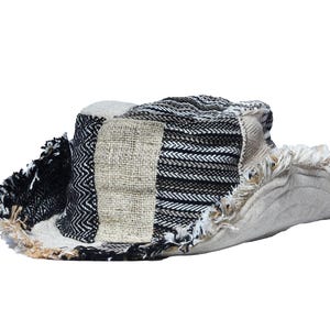 Könnte beinhalten: Ein Fischerhut mit einem Patchwork-Design aus schwarz-weiß gewebtem Stoff und hellbeigen Jute-Einsätzen. Der Hut hat eine ausgefranste, unebene Krempe und enthält den Text Himalayas Collectables in der oberen linken Ecke des Bildes.