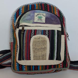May include: A colorful hemp backpack with a striped pattern in red, blue, green, and black. It features multiple zippered compartments, a small front pocket, and adjustable straps. The text "Himalaya Hemp" is visible on the front.