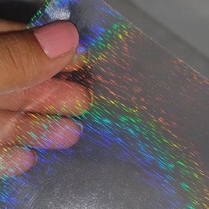 Puede incluir: Una lámina de vinilo holográfico iridiscente con un brillo arcoíris. El vinilo es transparente y tiene una textura sutil.