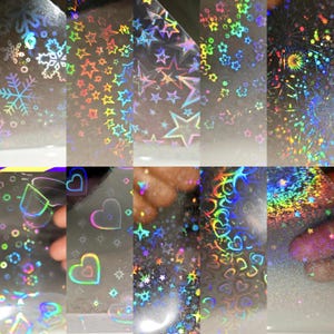 May include: A collection of ten transparent holographic overlay sheets featuring various patterns including snowflakes, stars, flowers, fireworks, hearts, and glitter, each reflecting a spectrum of rainbow colors when light hits the surface.