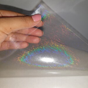 May include: A sheet of iridescent holographic vinyl with a rainbow sheen. The vinyl is clear and has a smooth, glossy finish.