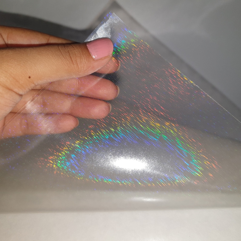 May include: A sheet of iridescent holographic vinyl with a rainbow sheen. The vinyl is clear and has a smooth, glossy finish.