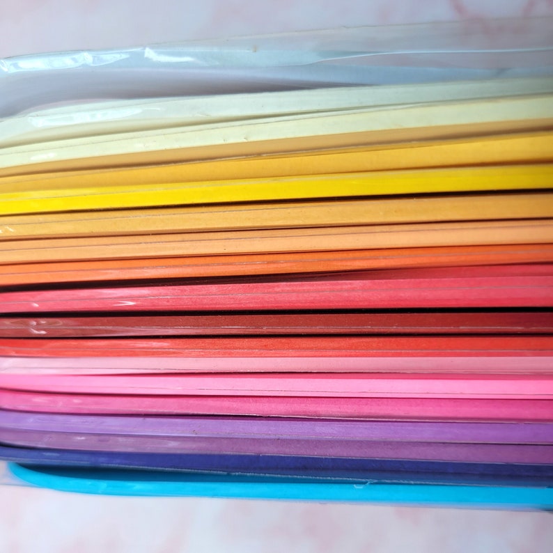 K&ouml;nnte beinhalten: Ein Stapel bunter Papierb&ouml;gen in einem Regenbogen-Farbverlauf, beginnend mit Hellblau und endend mit Dunkelblau. Das Papier ist in Klarsichtfolie verpackt.