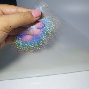 May include: A sheet of iridescent holographic film with a rainbow sheen. The film is translucent and has a subtle texture.