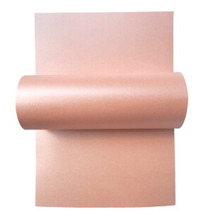 Op de afbeelding: Een vel lichtroze metallic papier opgerold. Het papier heeft een subtiele glans.