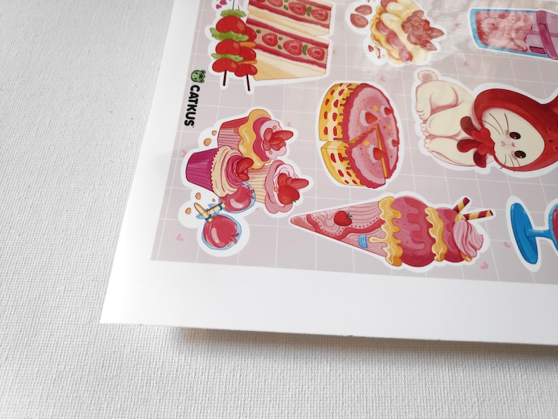 Puede incluir: Una hoja de pegatinas con varios postres de tem&aacute;tica de fresa, incluyendo cupcakes, porciones de pastel, conos de helado y un shortcake de fresa. Las pegatinas est&aacute;n impresas en vinilo transparente y tienen un acabado brillante.