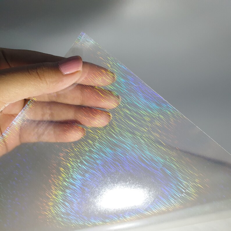 May include: A sheet of iridescent holographic film with a rainbow sheen. The film is clear and has a textured surface.