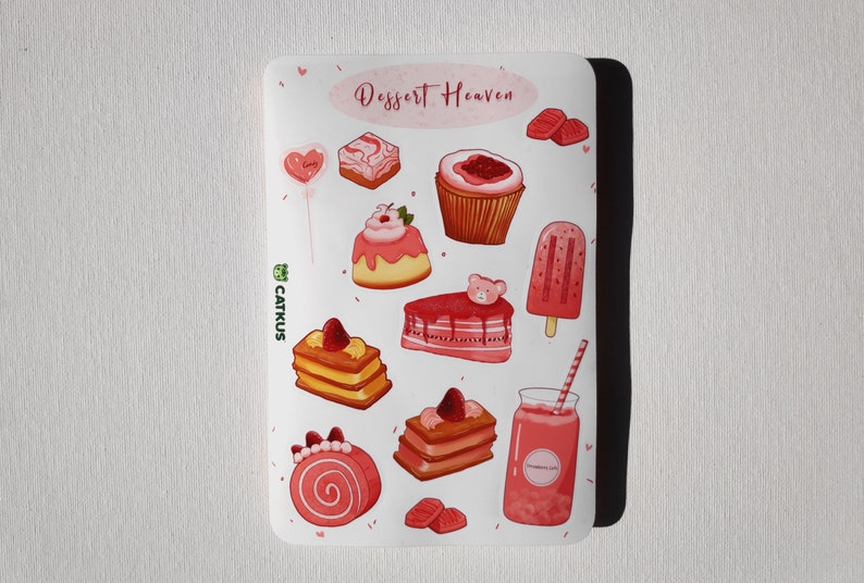 May include: A sheet of pink and white stickers featuring various desserts, including cakes, cupcakes, popsicles, and a strawberry smoothie. The stickers are decorated with hearts and the text "Dessert Heaven".