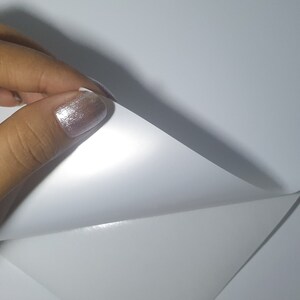 May include: A close-up of a white sheet of paper being folded in half. The paper is smooth and has a slight sheen.