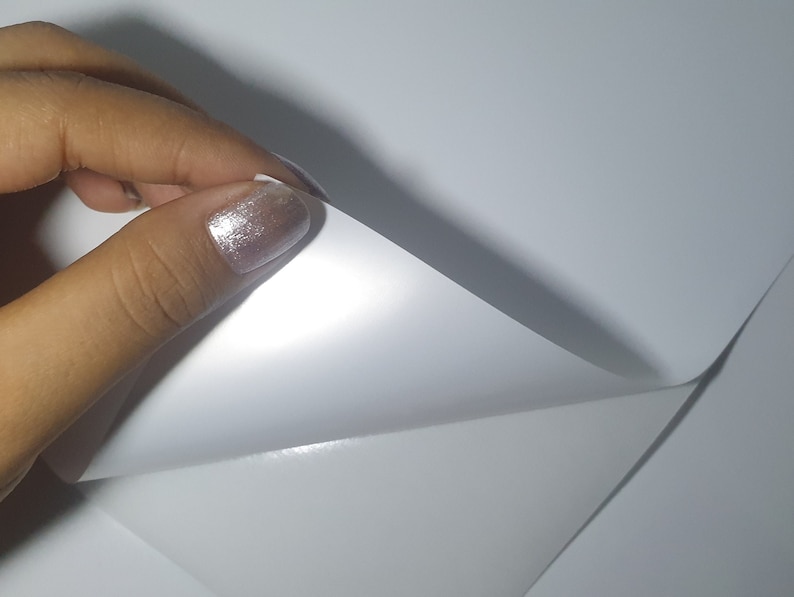 May include: A close-up of a white sheet of paper being folded in half. The paper is smooth and has a slight sheen.