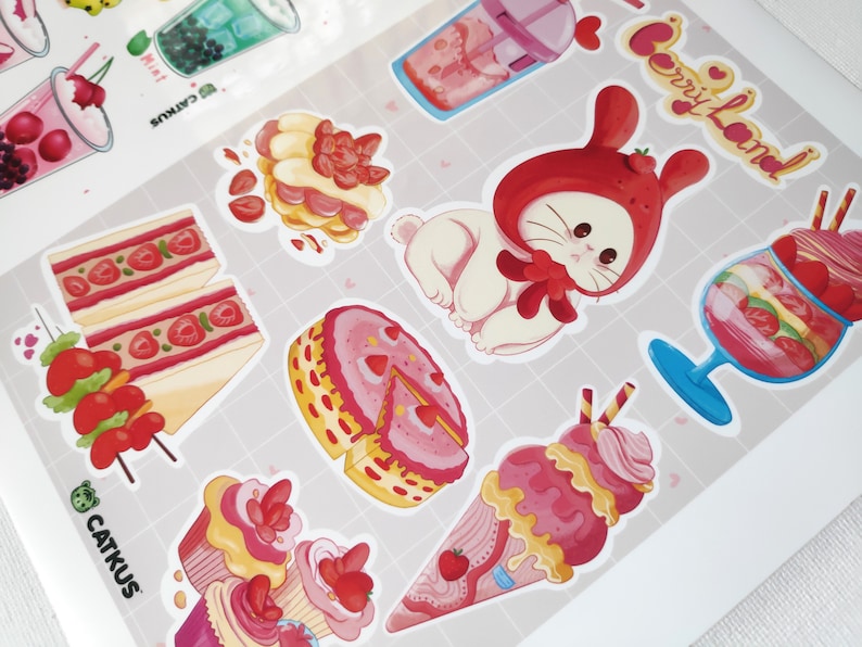 May include: A set of colourful stickers featuring a variety of sweet treats, including cakes, ice cream, and a bunny wearing a strawberry hat. The stickers are decorated with strawberries and hearts and have the text "Berry Land!" on one of the stickers.