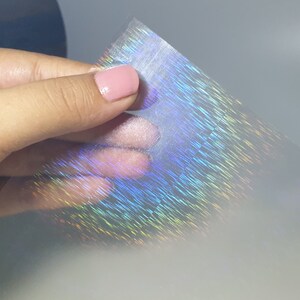May include: A sheet of iridescent holographic film with a rainbow pattern. The film is translucent and has a subtle texture.