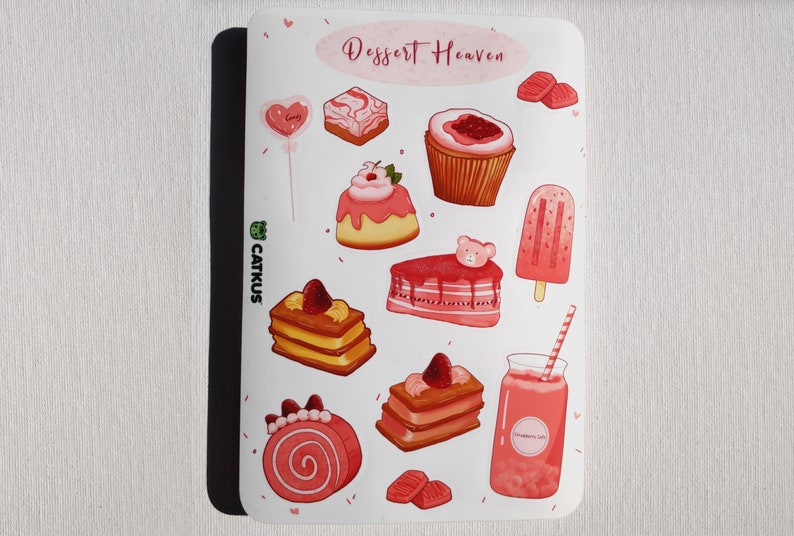 May include: A sheet of pink and white stickers featuring various desserts, including cakes, cupcakes, popsicles, and a milkshake. The stickers are decorated with hearts, sprinkles, and a bear. The text "Dessert Heaven" is at the top of the sheet.