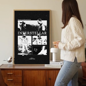 May include: A framed black and white movie poster for the film "Interstellar." The poster features images from the movie and the title "Interstellar" in large white letters. The poster is displayed on a wooden cabinet.