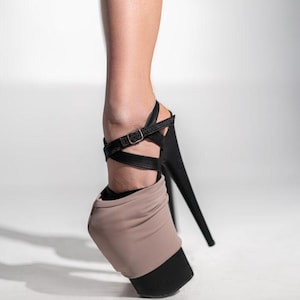 May include: Black high-heeled platform shoe with a black stiletto heel and a beige and black toe cover. The shoe has a black ankle strap with a buckle.