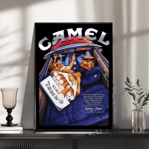 Puede incluir: Un anuncio de Camel enmarcado que muestra el interior de un coche cl&aacute;sico con dos figuras y un paquete de cigarrillos. El logotipo de Camel est&aacute; en la parte superior. La imagen tiene un fondo negro y un marco negro.