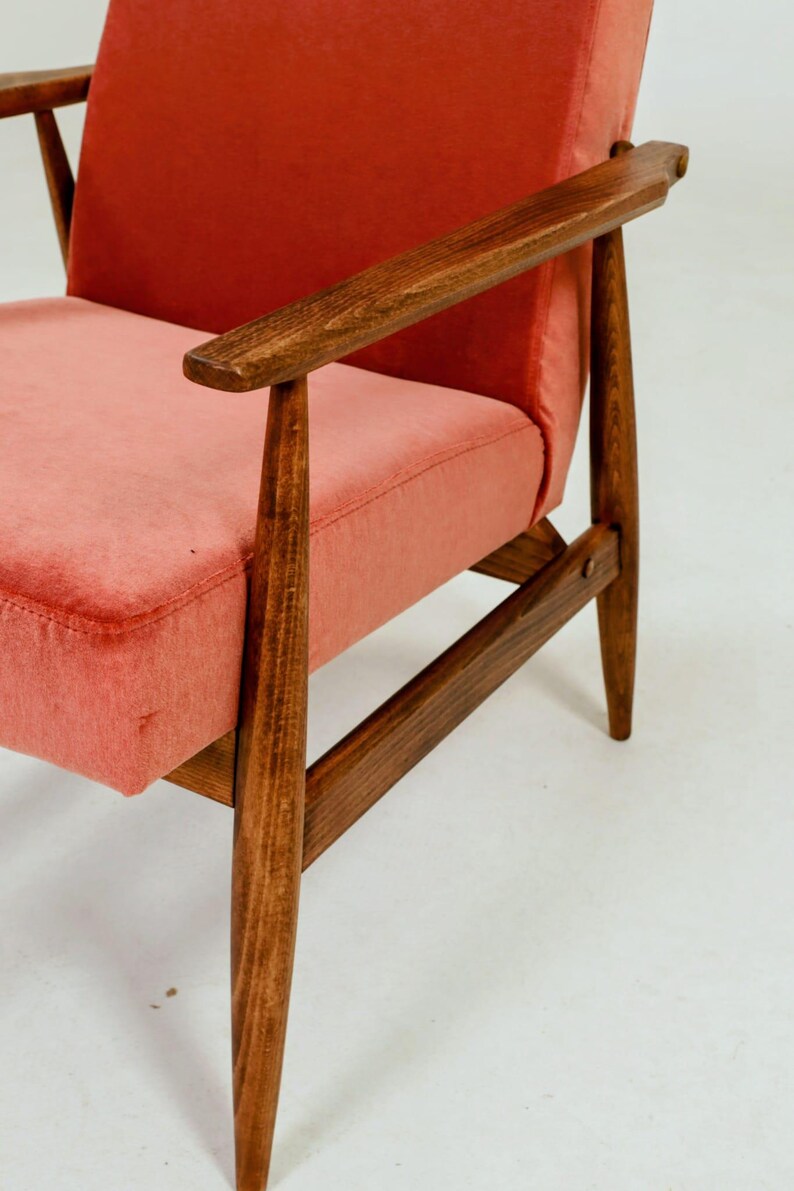 May include: Mid-century modern armchair with a coral-colored seat and backrest. The wooden frame and armrests are a dark brown. The chair has a classic, minimalist design, perfect for living room or bedroom decor.