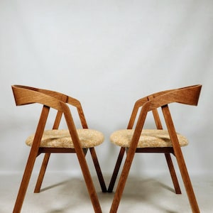Può includere: Due sedie in legno con una finitura marrone chiaro e un design geometrico. Le sedie hanno una seduta imbottita con un tessuto a fantasia marrone chiaro e bianco.