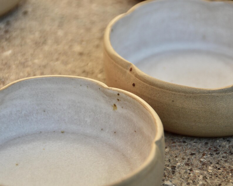 May include: Two white ceramic bowls with a slightly textured surface. The bowls have a rounded shape with a slightly flared rim.