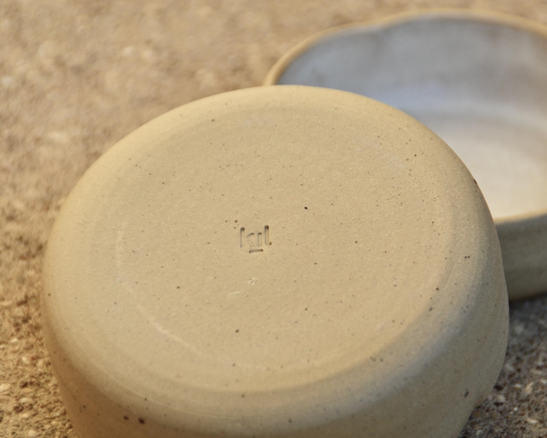 May include: A beige ceramic bowl with a rough texture and a small, stamped mark on the bottom that reads "Icil."