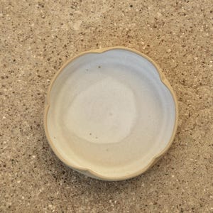 May include: A white ceramic bowl with a scalloped edge. The bowl is slightly off-white and has a subtle texture.