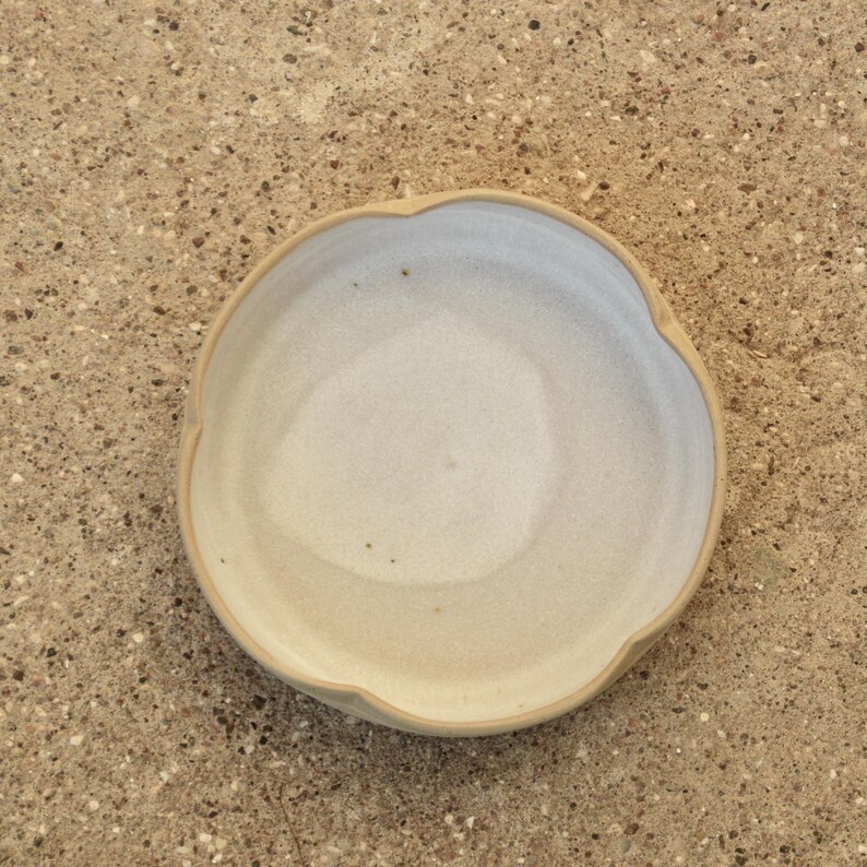 May include: A white ceramic bowl with a scalloped edge. The bowl is slightly off-white and has a subtle texture.