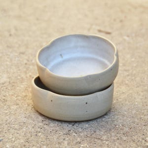 May include: Two stacked ceramic bowls with a light beige glaze. The bowls have a slightly irregular, wavy rim.