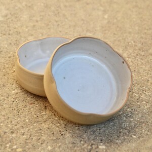 May include: Two ceramic bowls with a white glaze and a light brown rim. The bowls are slightly scalloped and have a rustic, handmade look.